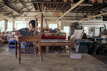 熟练的家具制造商在他的大型木工车间独自工作时,在工作台上打磨一把